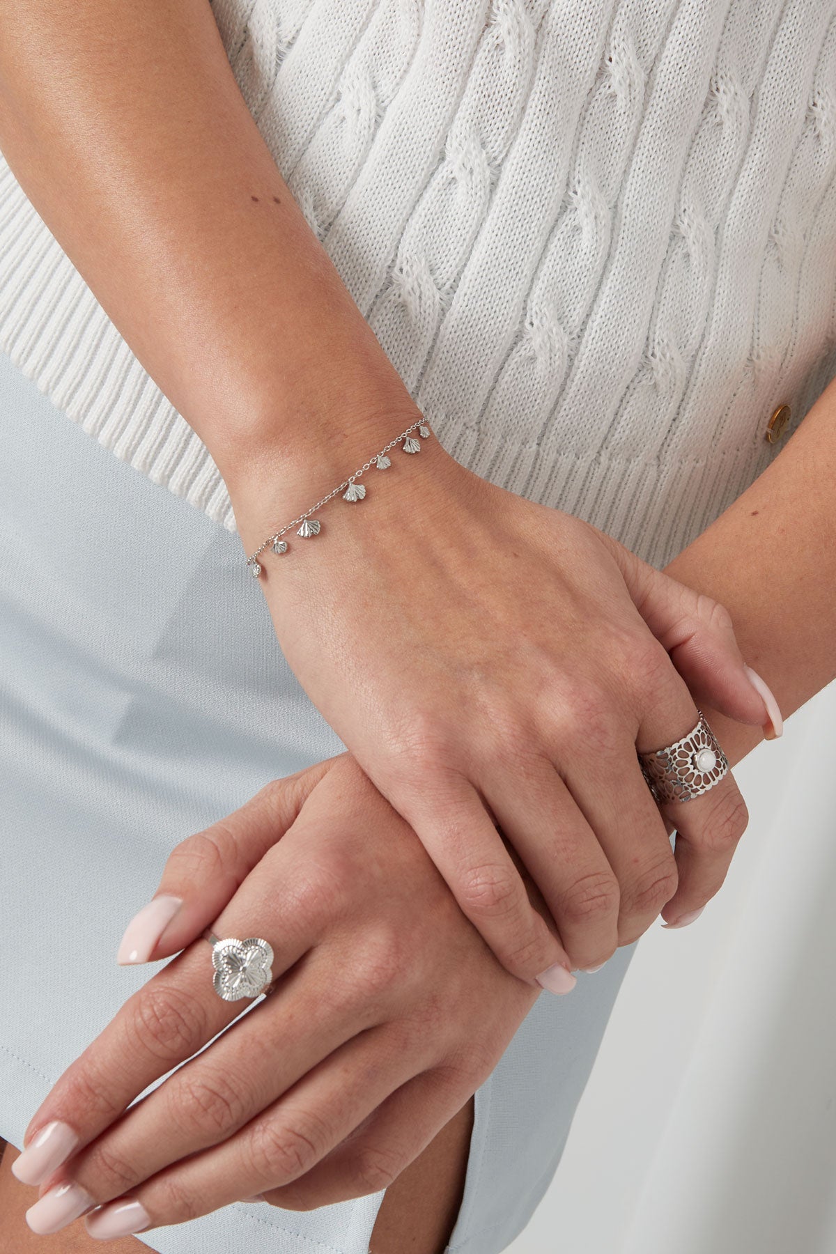 Woman wearing the silver ginkgo leaf charm bracelet paired with stylish rings, dressed in a light knit sweater and blue skirt