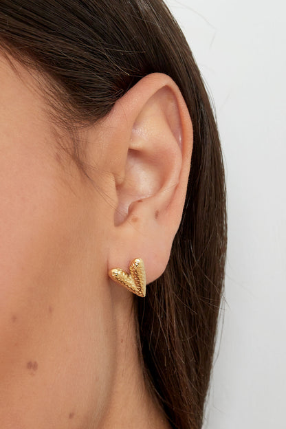 Side profile close-up of a woman’s ear wearing a gold textured heart-shaped stud earring