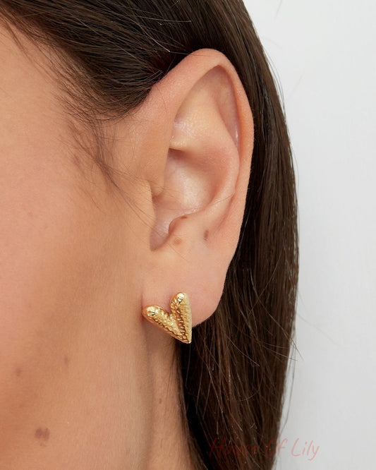 Side profile close-up of a woman’s ear wearing a gold textured heart-shaped stud earring