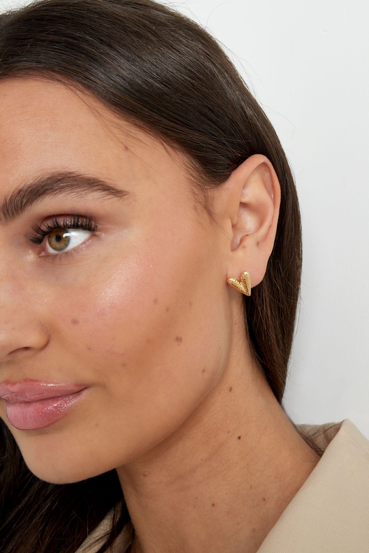Close-up angled view of a woman wearing the gold heart stud earring, showcasing the hammered texture