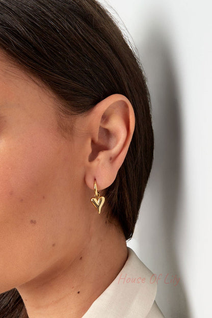 Close-up side profile of a woman wearing gold heart-shaped drop earrings, highlighting detail and fit