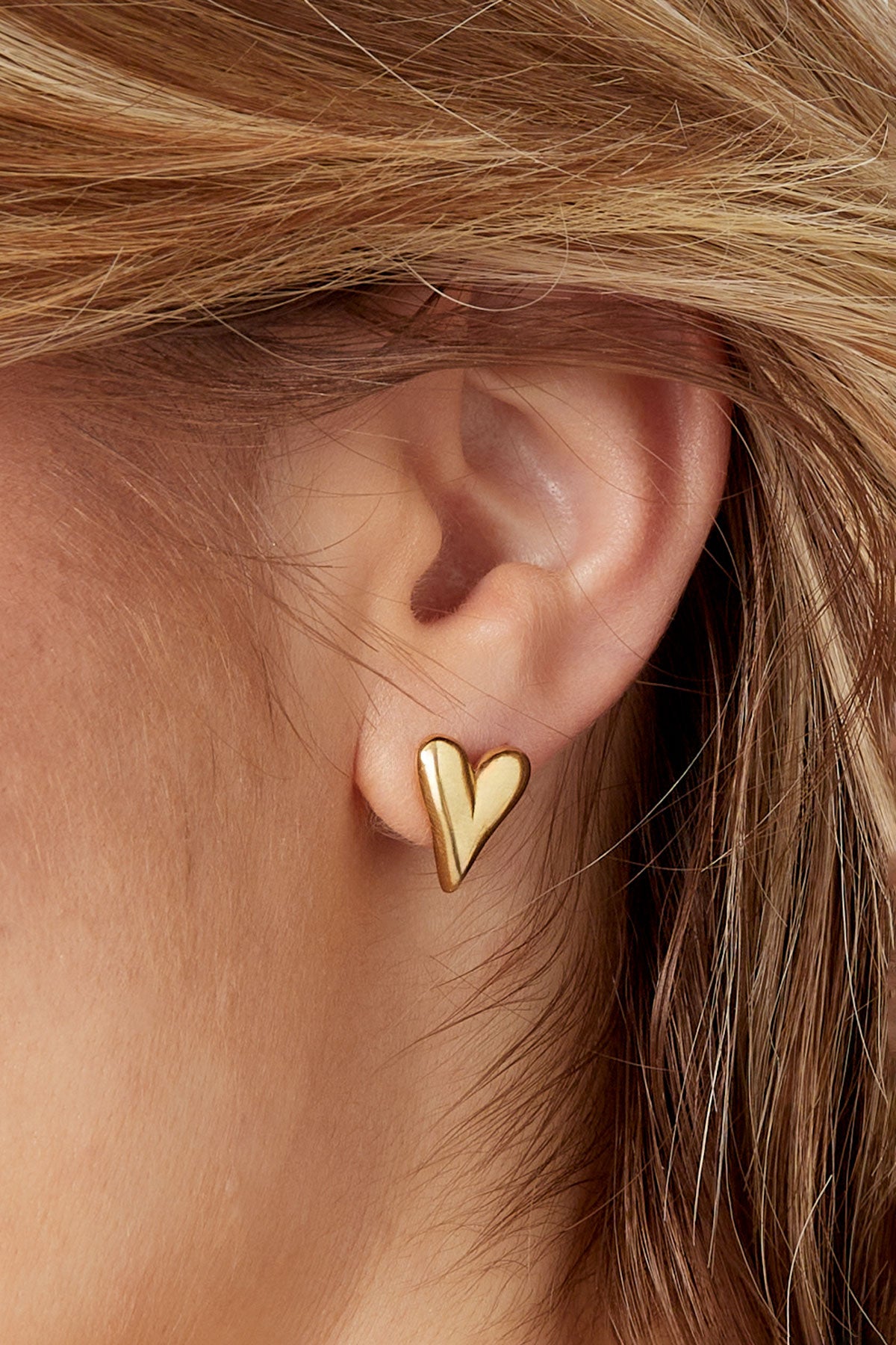 Close-up of ear adorned with gold heart stud earring showcasing smooth, polished minimal design