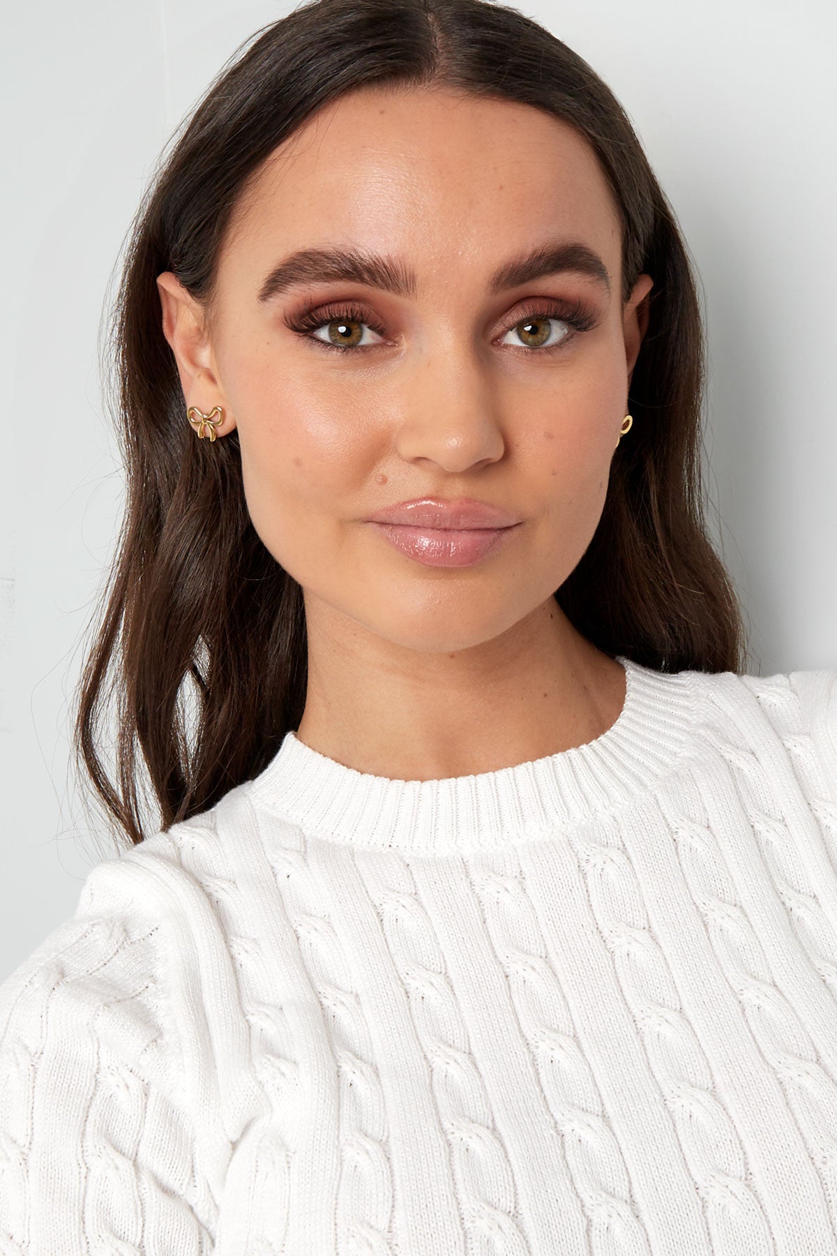 Model wearing gold bowknot stud earrings with white cable knit sweater