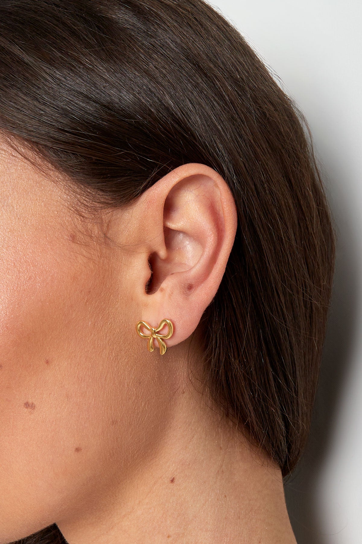 Close-up side view of model's ear wearing a gold bowknot stud earring