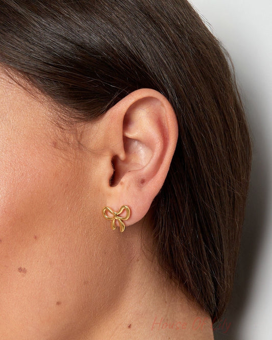 Close-up side view of model's ear wearing a gold bowknot stud earring