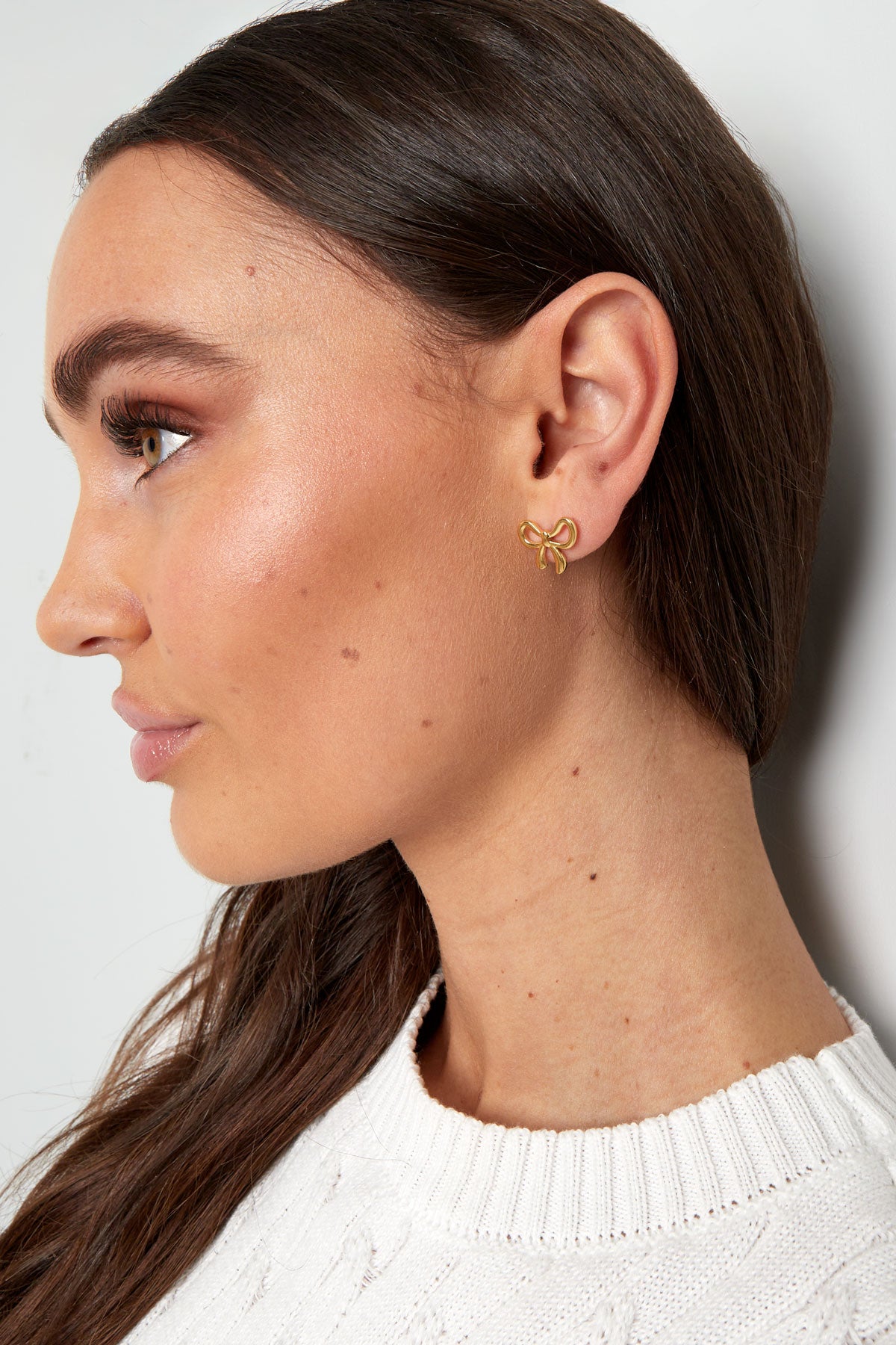 Side profile of model wearing gold bowknot stud earrings showcasing elegant fit