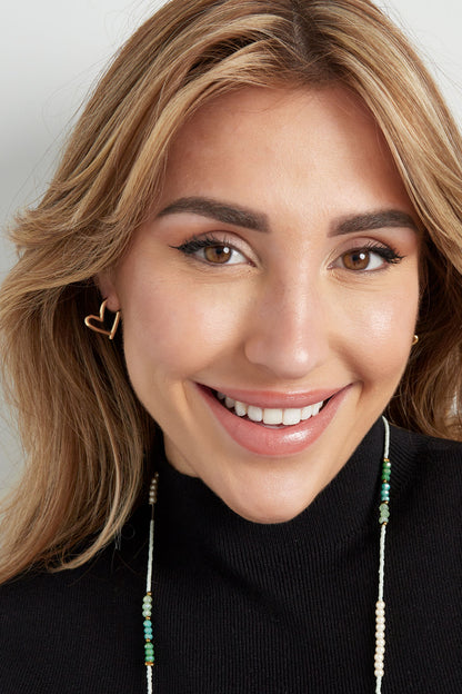 Smiling woman wearing gold heart-shaped hoop earrings and a beaded necklace