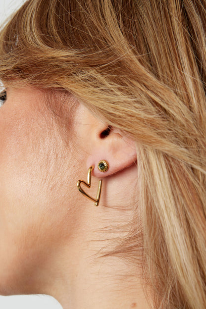 Close-up of woman's ear wearing gold heart hoop earrings with a small green stud earring