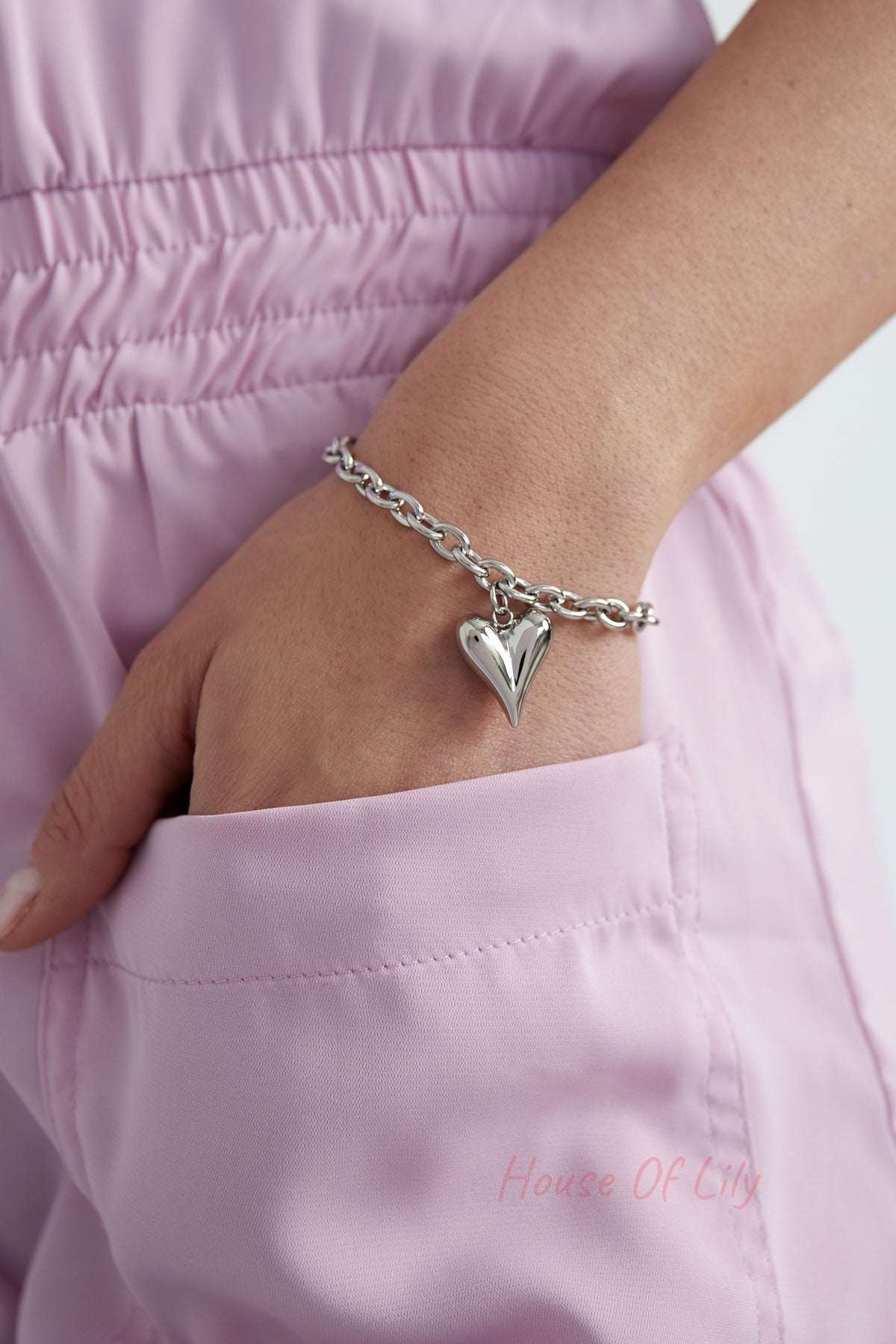 Close-up of silver chunky heart charm bracelet worn on wrist with pink outfit pocket detail
