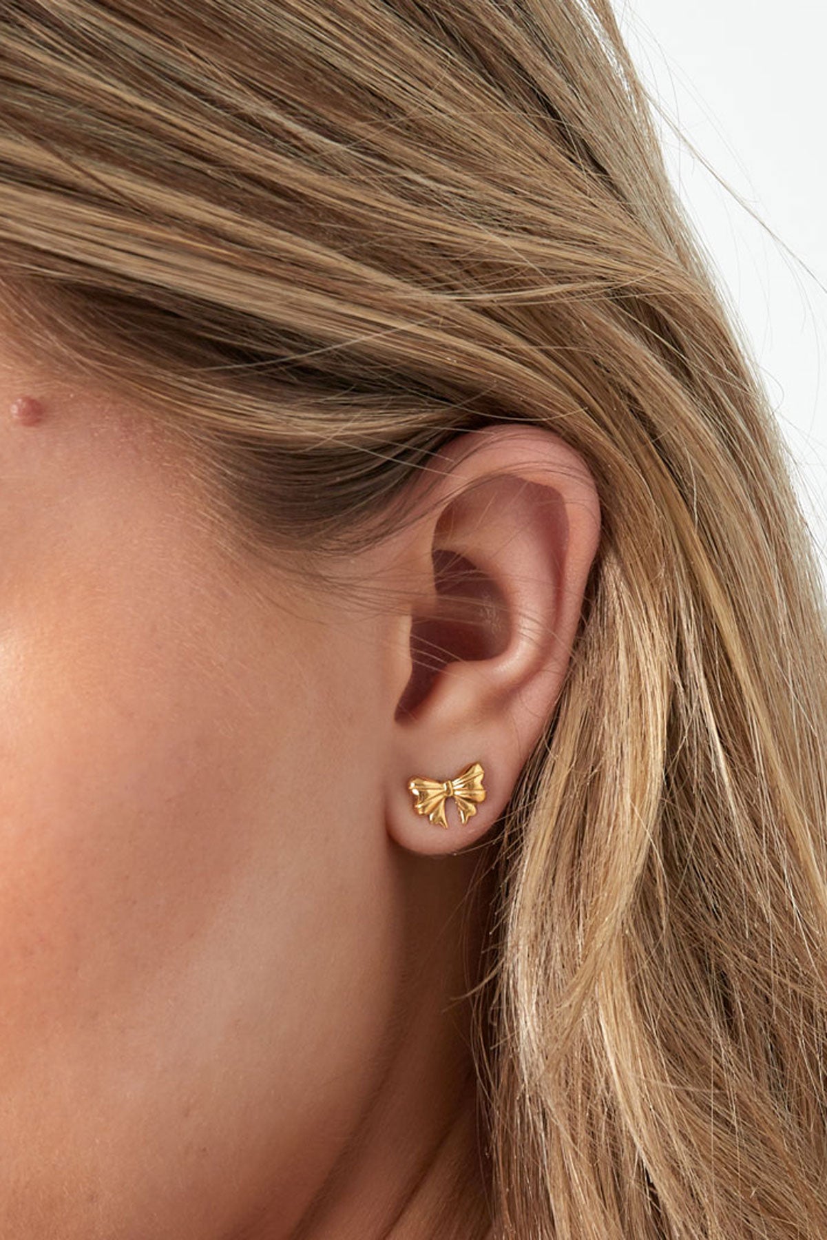 Close-up of the same model's ear highlighting the gold bow stud earring with detailed view