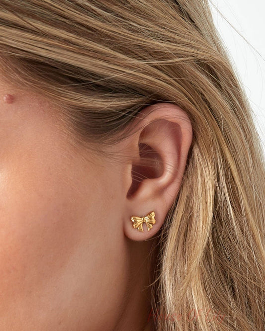 Close-up of the same model's ear highlighting the gold bow stud earring with detailed view