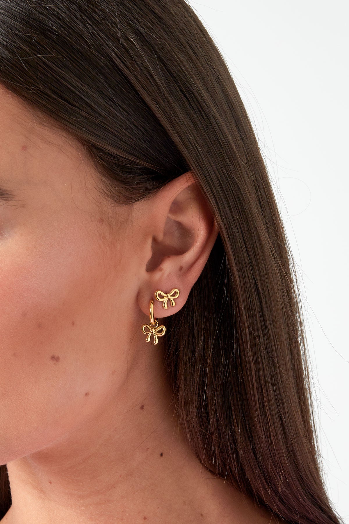 Close up of a woman's ear wearing a gold bow knot stud earring and matching bow knot dangling hoop earring
