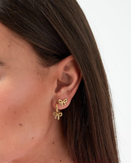 Close up of a woman's ear wearing a gold bow knot stud earring and matching bow knot dangling hoop earring