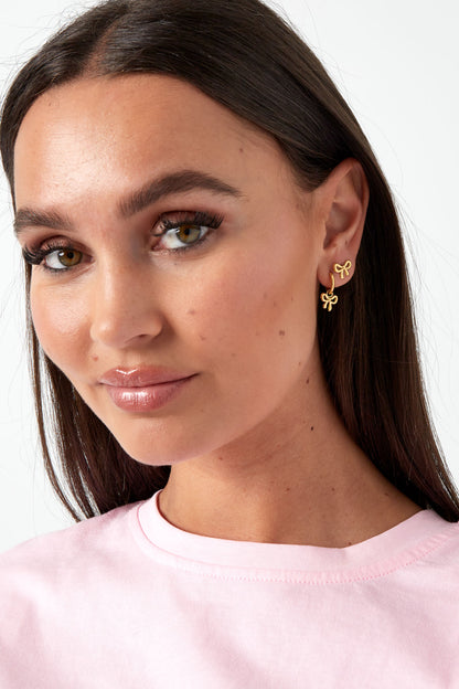Model wearing gold bow hoop earrings paired with matching bow stud earrings