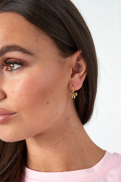 Close-up of model's ear showing gold bow hoop earrings and bow stud earrings