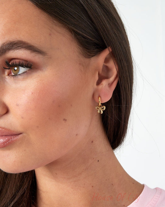 Close-up of model's ear showing gold bow hoop earrings and bow stud earrings