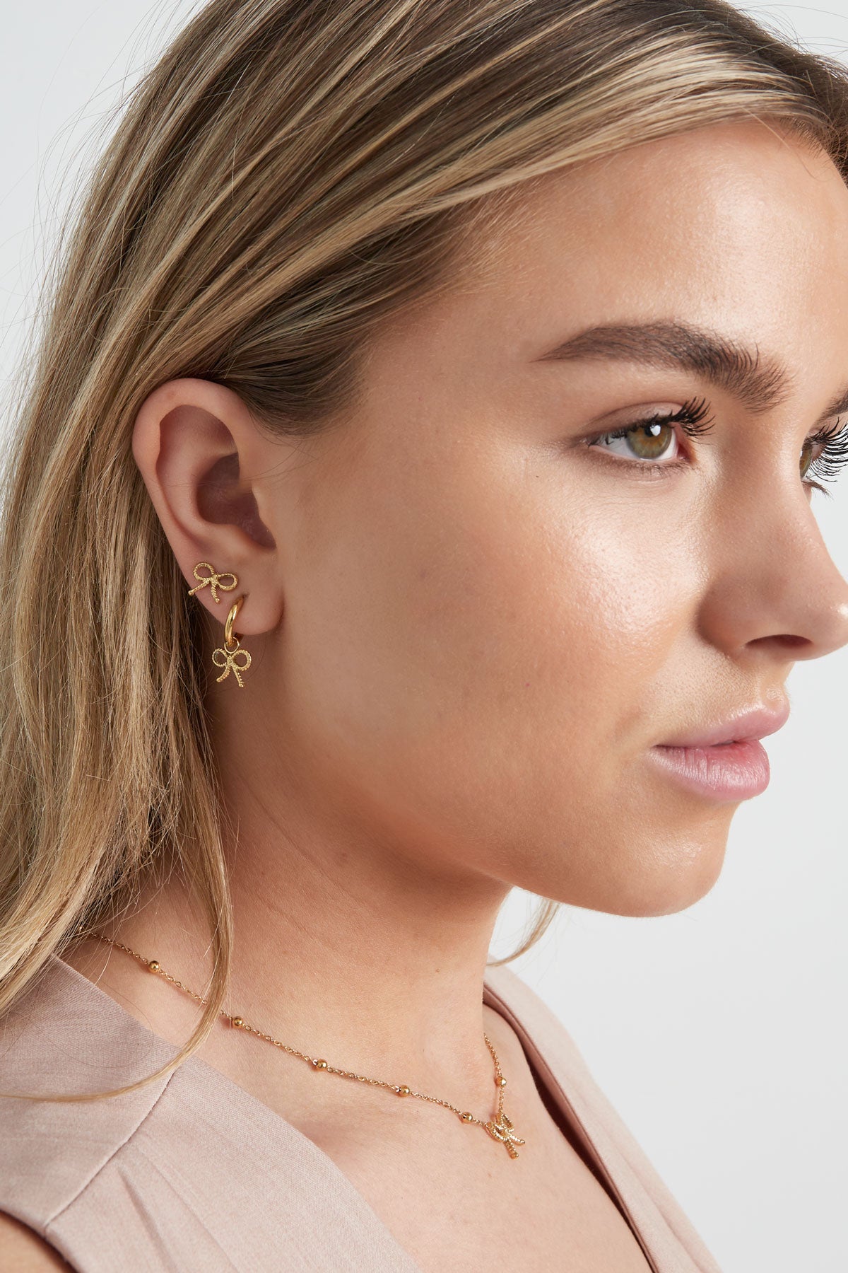 Close-up side profile of woman wearing gold bow hoop earrings and matching bow stud earrings