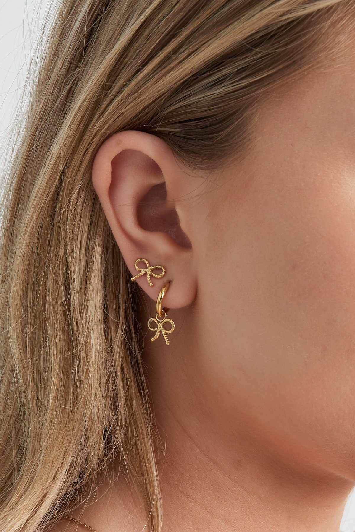 Close-up of woman’s ear wearing a gold hoop earring with bow charm alongside a matching bow stud
