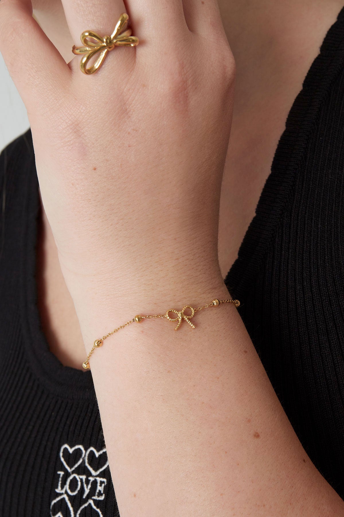 Woman wearing gold-tone delicate bow charm bracelet and matching bow ring with black top