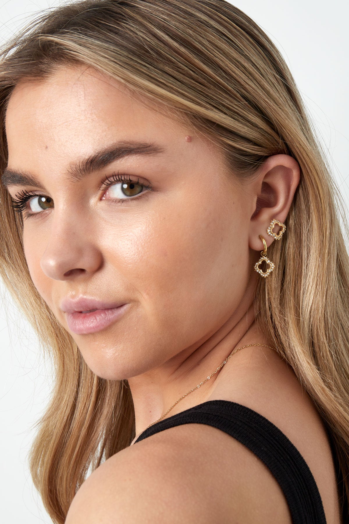 Close-up of woman wearing gold sparkle clover stud earrings paired with matching dangling earrings