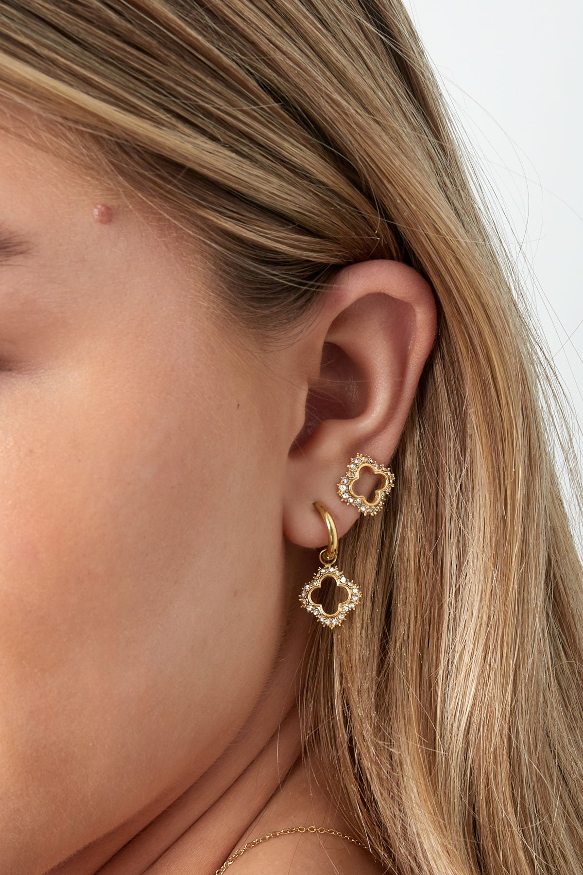 Side close-up of woman's ear showing gold sparkly open clover stud and matching drop earring