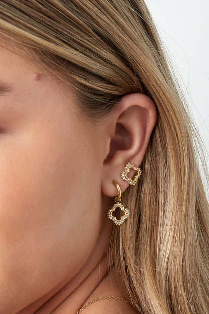 Side close-up of woman's ear showing gold sparkly open clover stud and matching drop earring