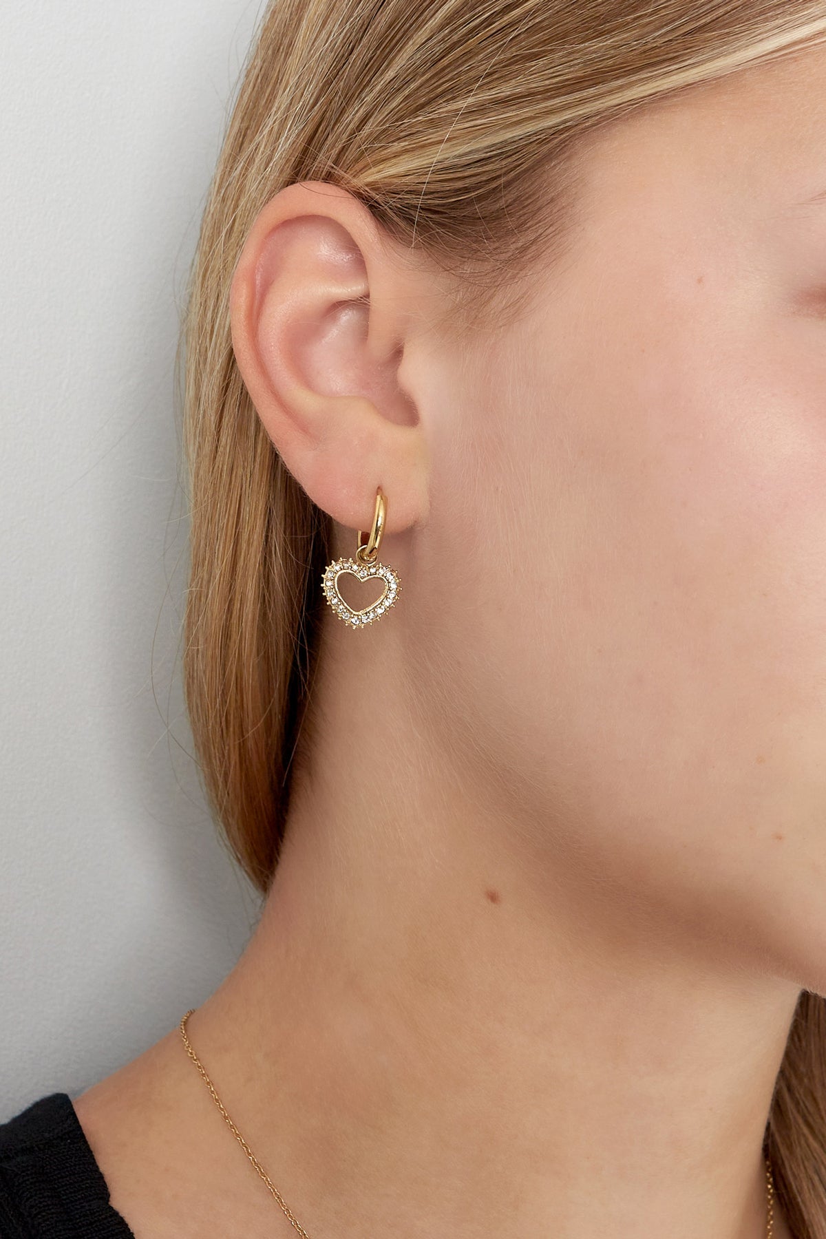 Close-up of a woman wearing gold-tone heart-shaped rhinestone drop earring with hoop closure