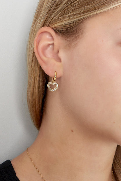 Close-up of a woman wearing gold-tone heart-shaped rhinestone drop earring with hoop closure
