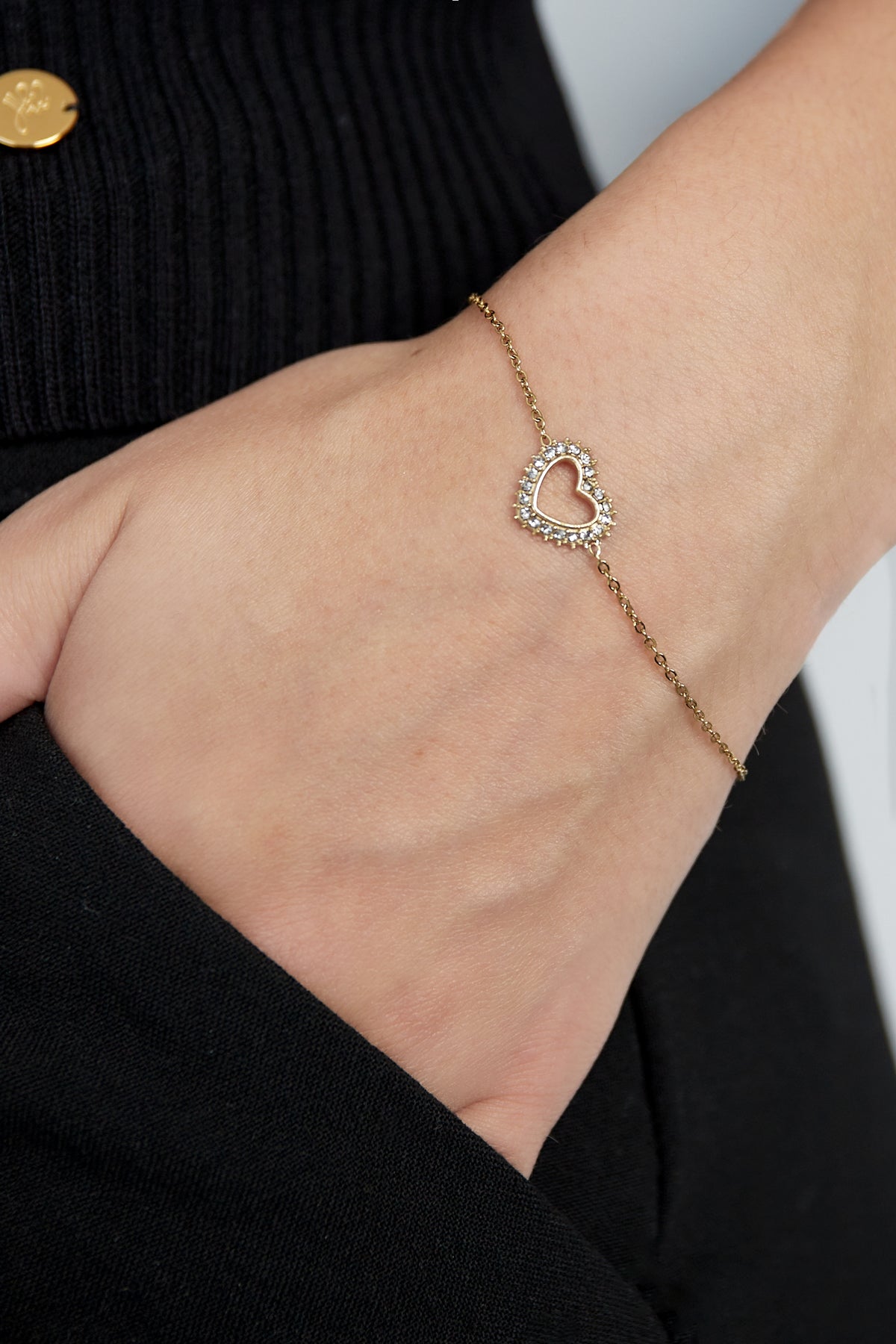 Close-up of a woman wearing a gold-tone heart charm bracelet with rhinestones on her wrist showcasing its delicate design