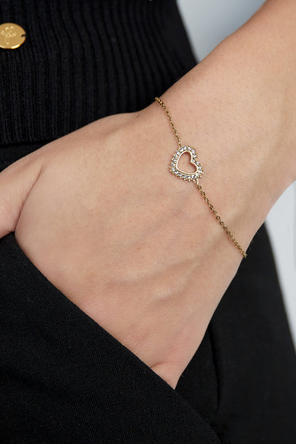 Close-up of a woman wearing a gold-tone heart charm bracelet with rhinestones on her wrist showcasing its delicate design