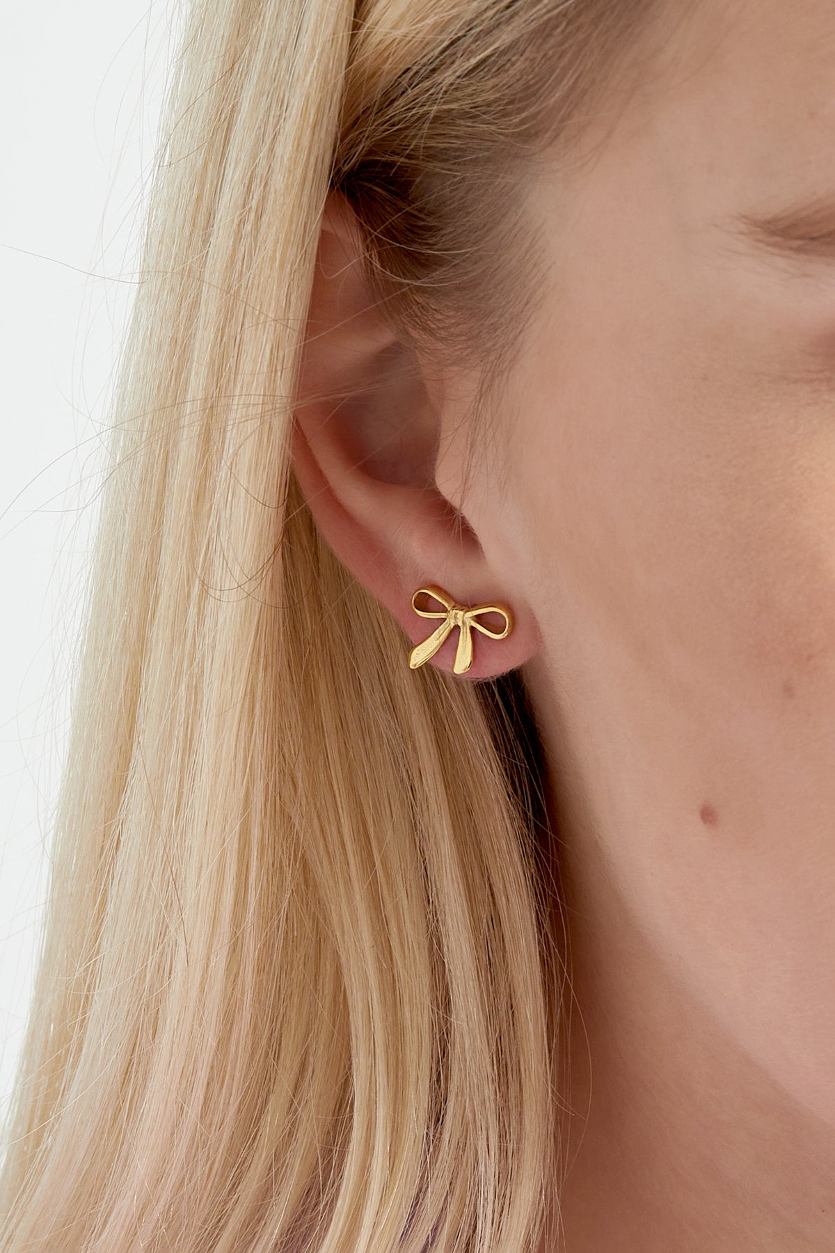 Close-up side view of woman wearing gold bow stud earrings on blonde hair