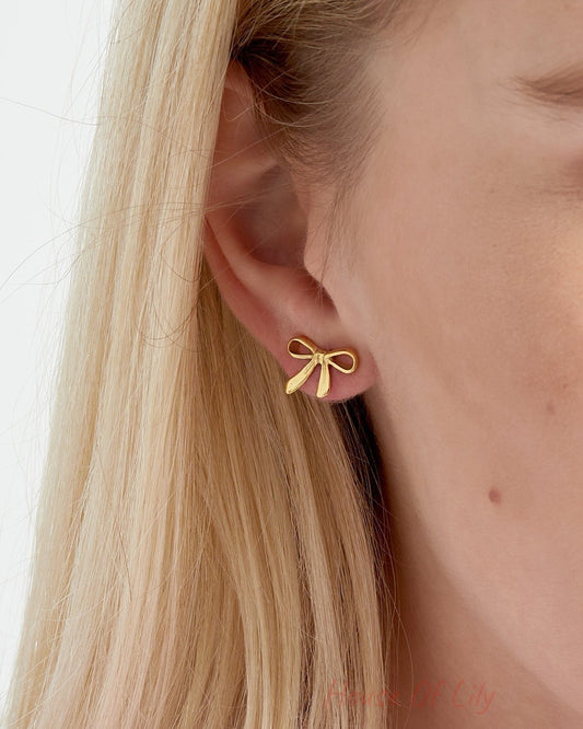 Close-up side view of woman wearing gold bow stud earrings on blonde hair