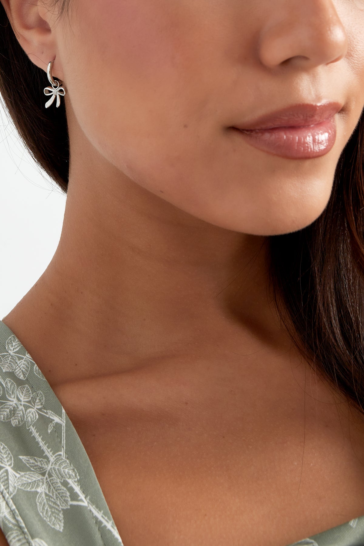 Close-up of woman wearing silver bow charm hoop earring, side view