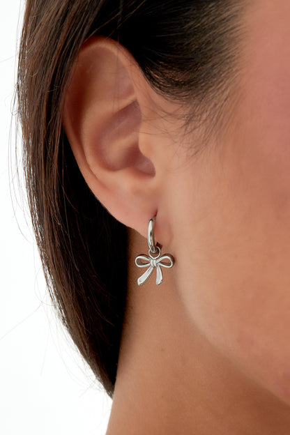 Close-up of woman wearing silver bow charm hoop earring, front view with green leafy top