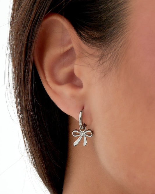 Close-up of woman wearing silver bow charm hoop earring, front view with green leafy top