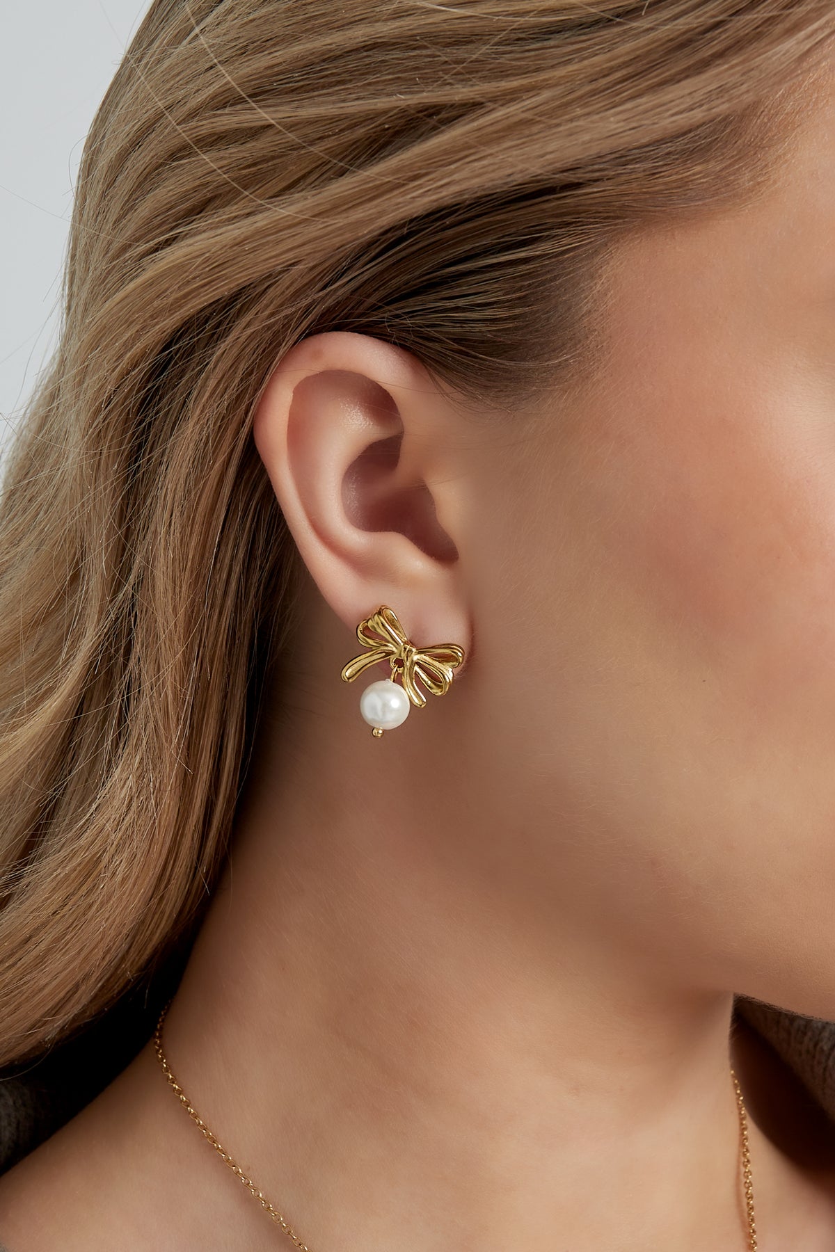 Close-up of woman wearing gold bow earrings with pearl drops showing youthful, minimal style