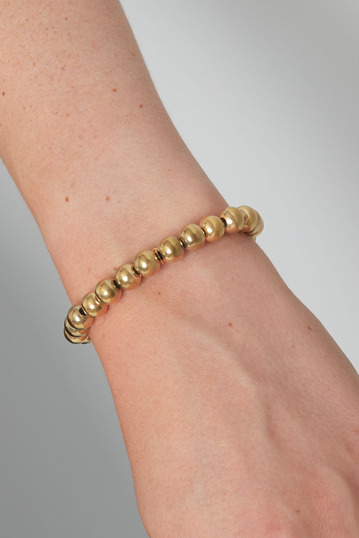 Close-up of a woman's wrist wearing a gold beaded bracelet showing smooth, shiny bead details