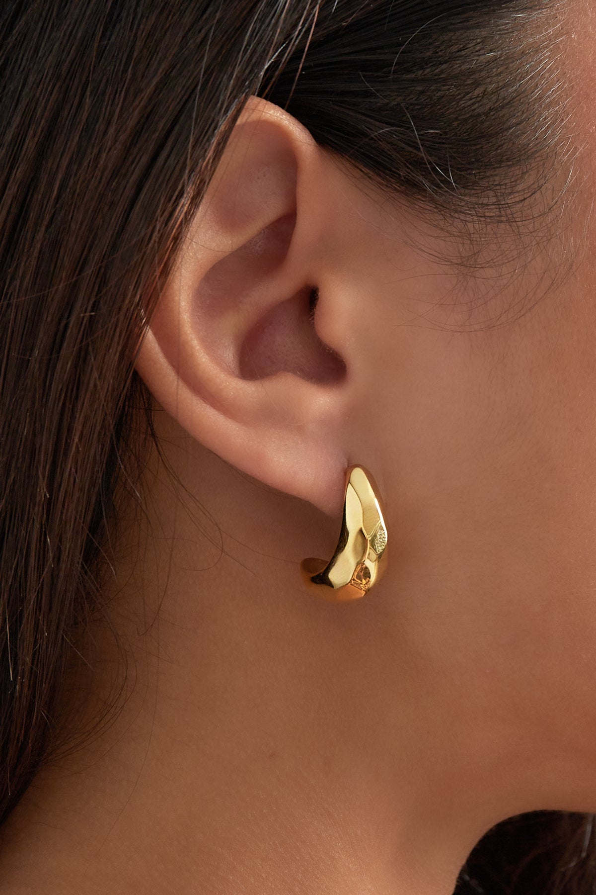 Detailed side view of gold pebble hoop earring worn on woman’s ear