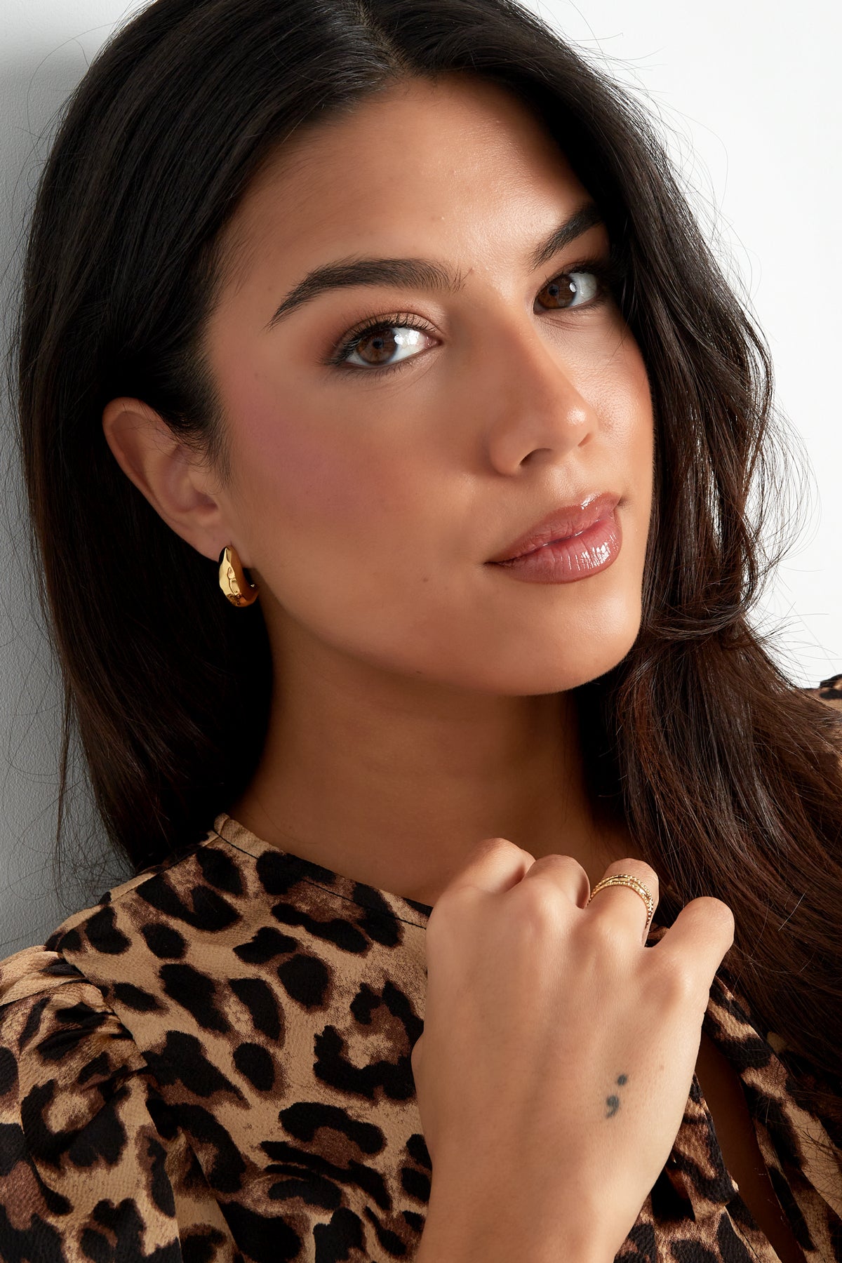 Portrait of a woman wearing gold pebble hoop earrings and matching rings, leopard print top