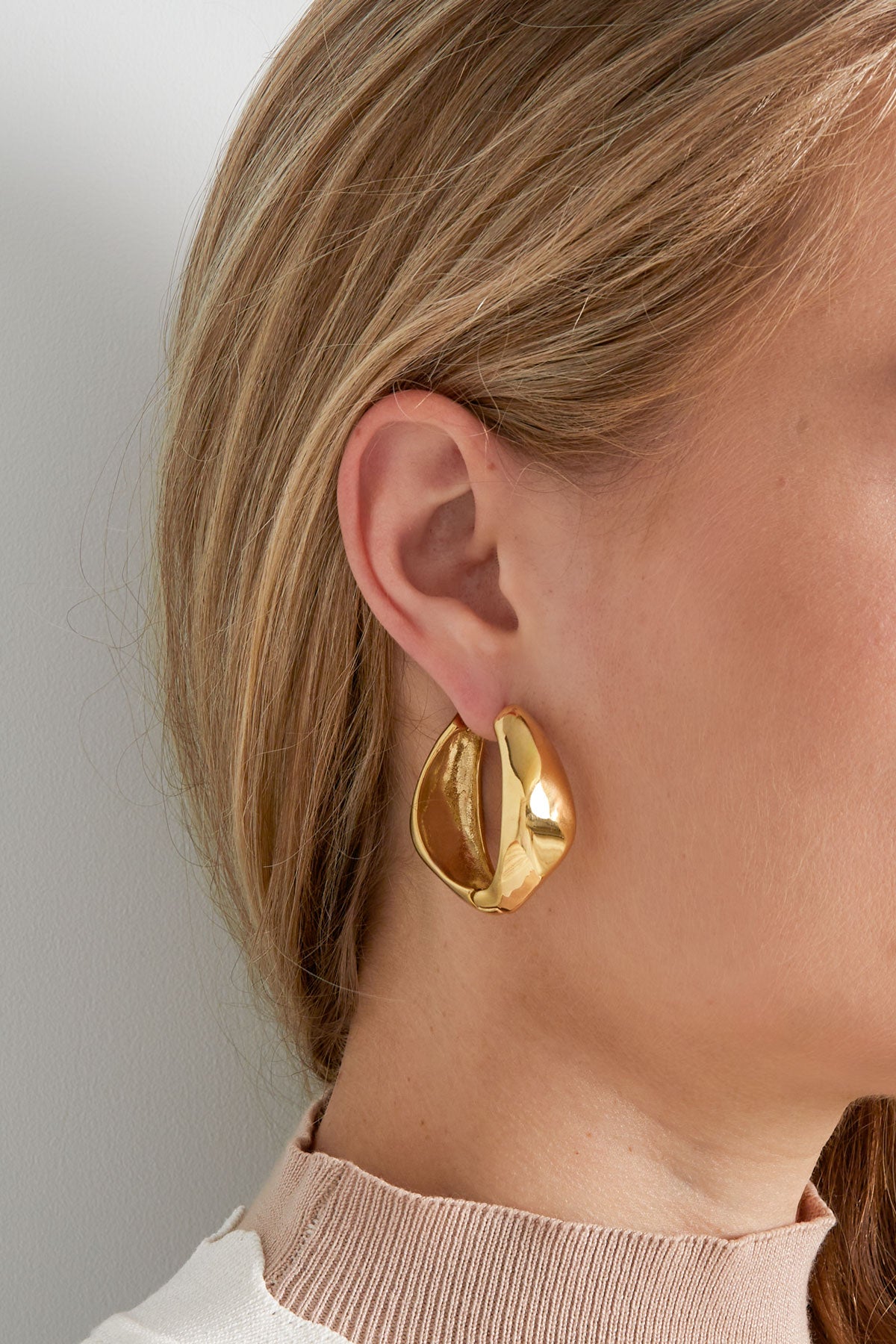 Close-up of gold twist hoop earring worn by a woman, highlighting the smooth, twisted form on ear.