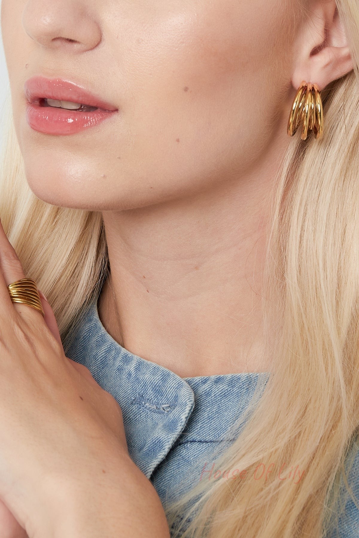 Close-up of model wearing gold triple loop hoop earrings paired with matching ring and denim shirt