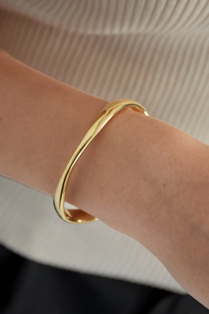 Close-up of wrist wearing sleek gold cuff bracelet showing soft curved design and smooth finish