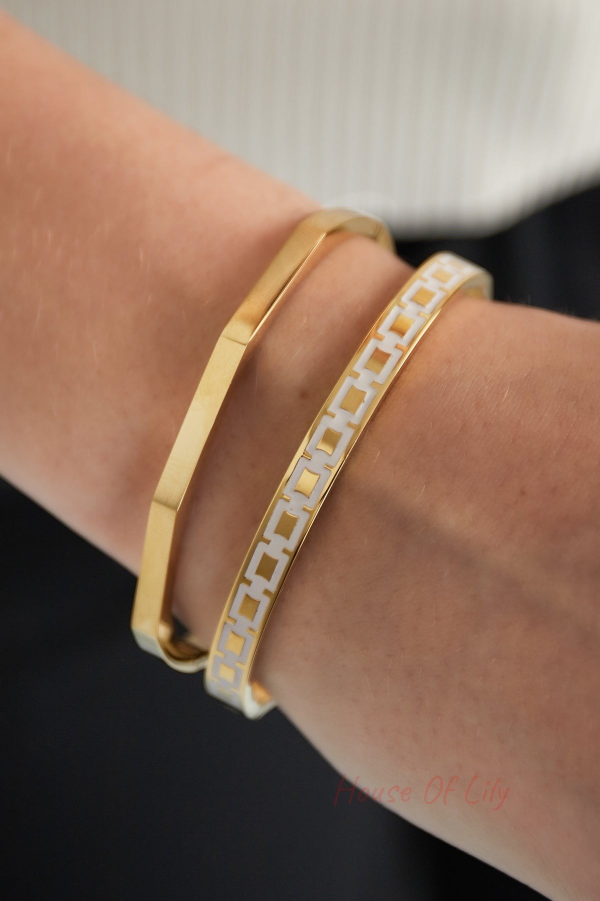 Close-up of wrist wearing two bracelets: gold hexagon bangle and white and gold patterned bracelet