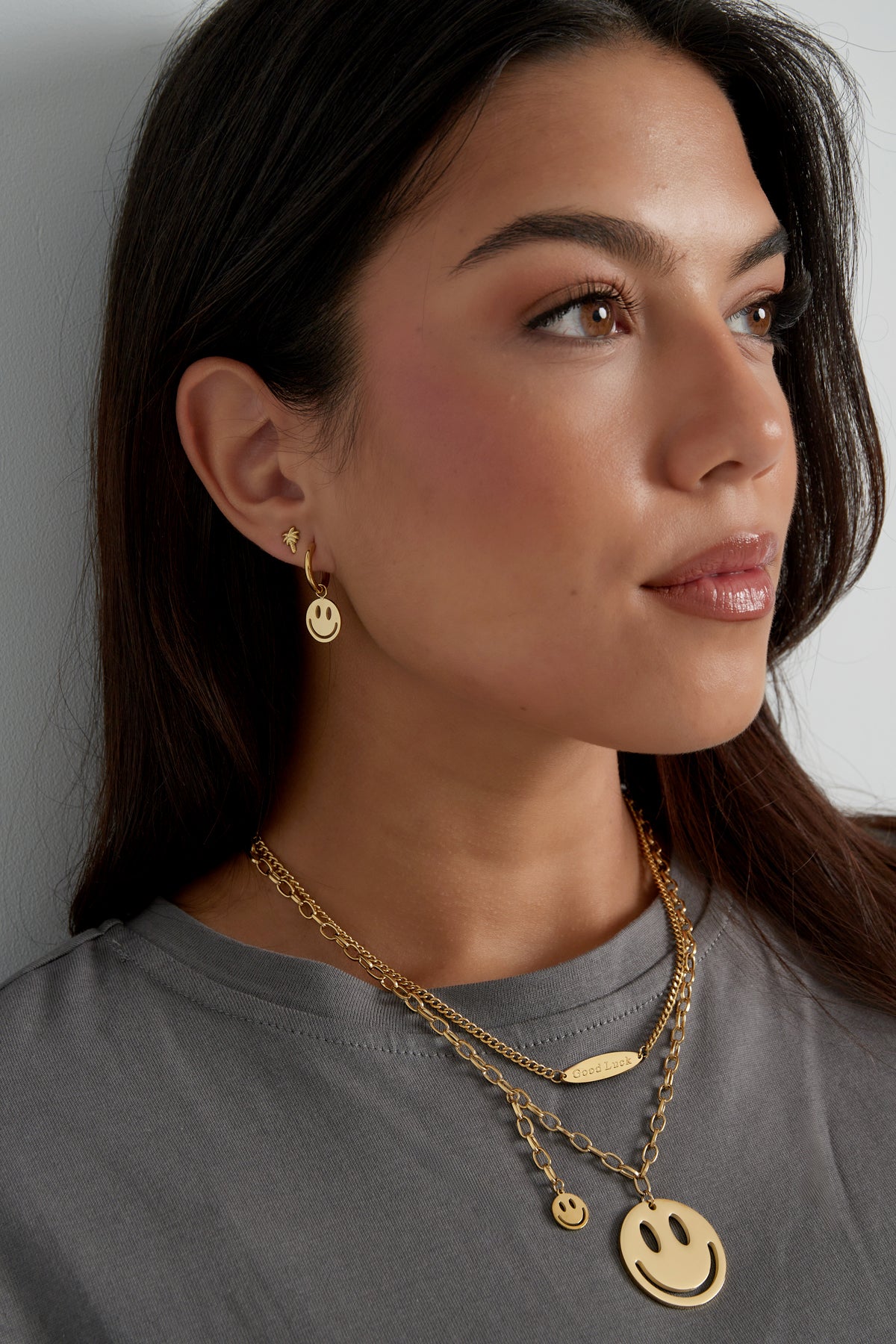 Another close-up view of the woman showing the gold smiley face hoop earring and layered necklaces with smiley pendants