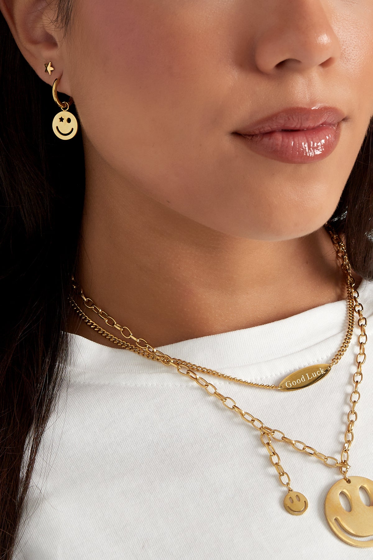 Close-up showing gold smiley face hoop earring worn with layered gold necklaces and star stud earring
