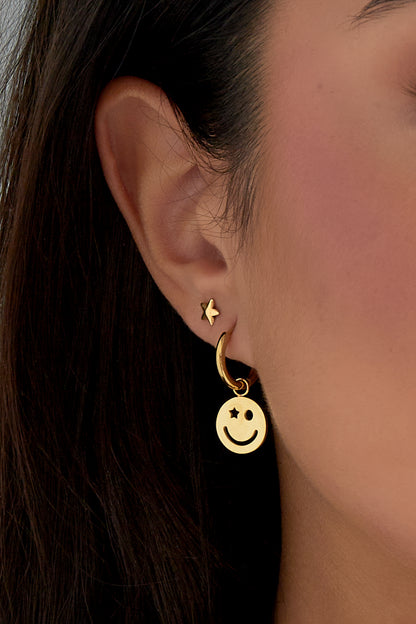 Side profile of woman wearing gold smiley face hoop earring and matching star stud earring