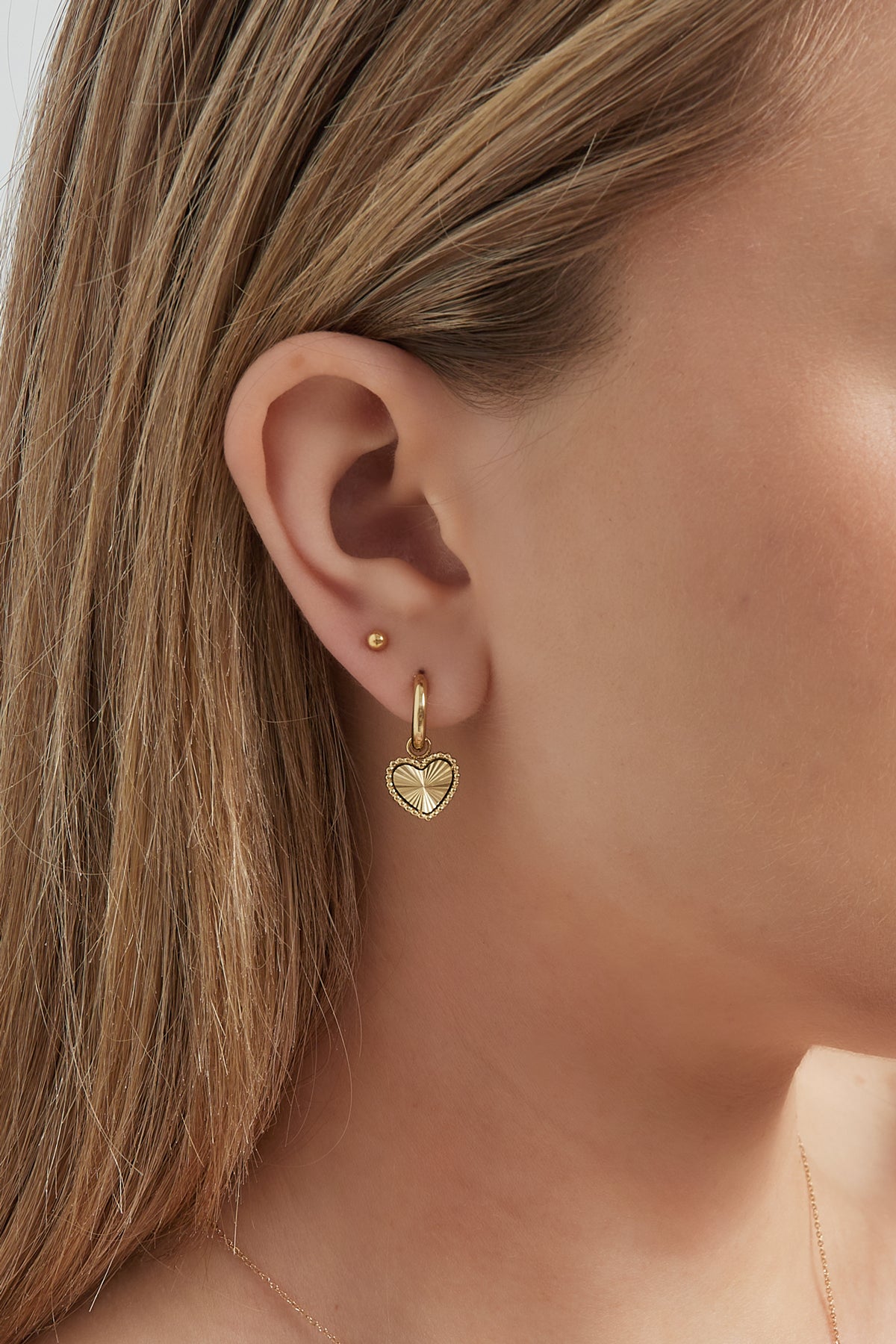 Close-up of a woman wearing gold hoop earrings with sunburst heart charms showcasing their size and fit