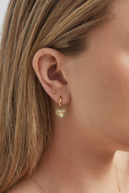 Close-up of a woman wearing gold hoop earrings with sunburst heart charms showcasing their size and fit