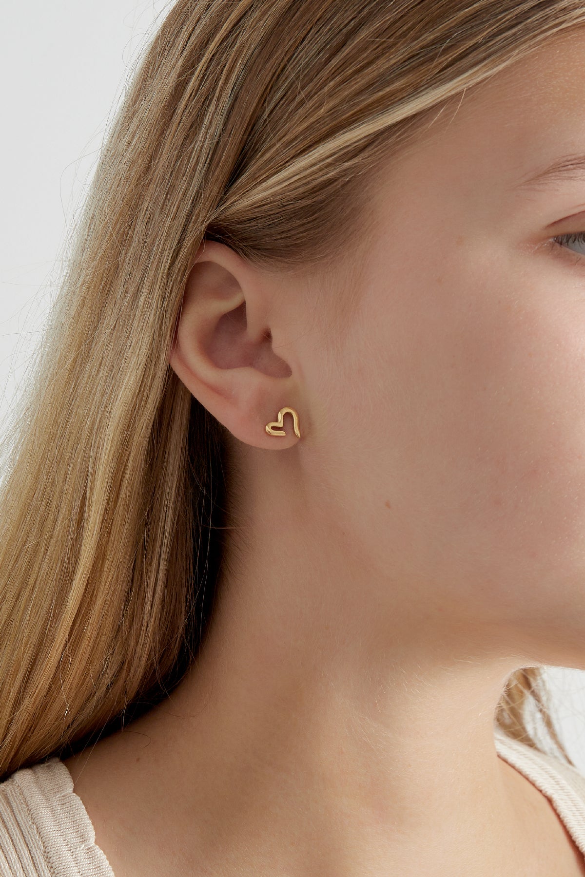 Close-up side view of gold-tone open heart stud earring worn on woman's ear with light skin and blonde hair