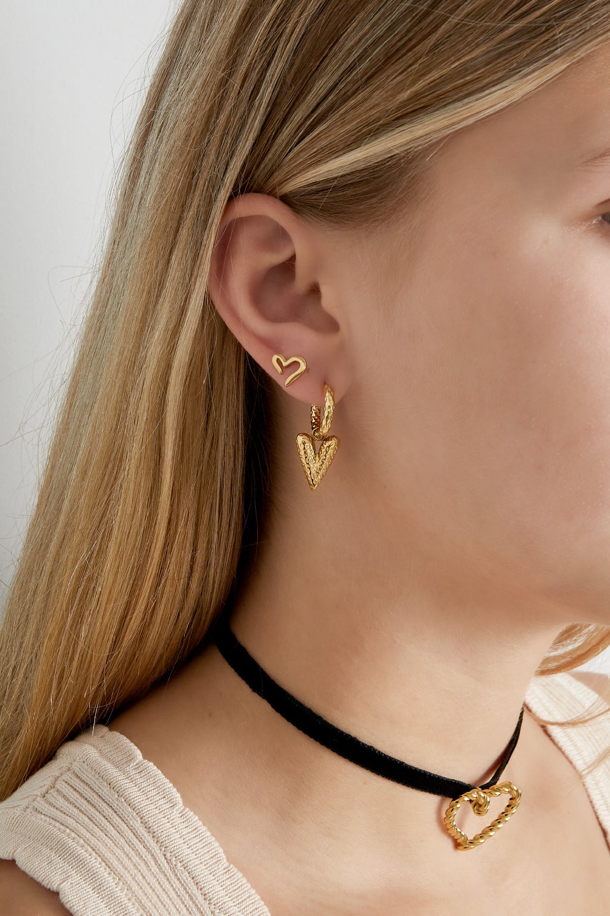 Gold-tone open heart stud earrings styled with additional textured heart drop earrings and black choker necklace on woman